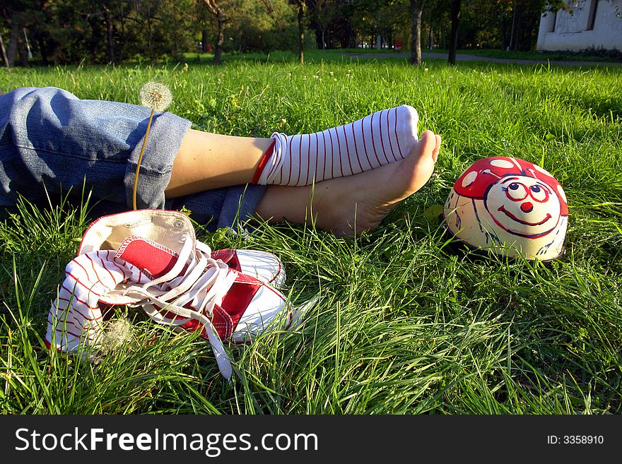 View of girl's legs and her feet on grass next to pair of athletic shoes. Face of girl not in photo. View of girl's legs and her feet on grass next to pair of athletic shoes. Face of girl not in photo.