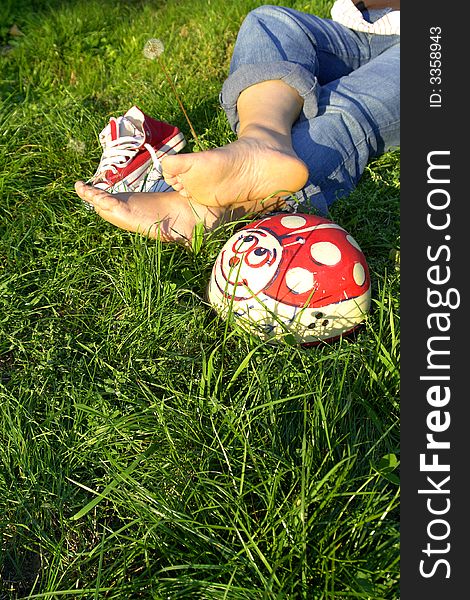 View of girl's legs and her bare feet on grass next to pair of athletic shoes. Face of girl not in photo. View of girl's legs and her bare feet on grass next to pair of athletic shoes. Face of girl not in photo.