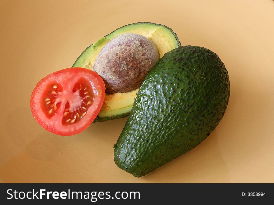 Avocados in half with a slice of tomato on a yellow plate. Avocados in half with a slice of tomato on a yellow plate