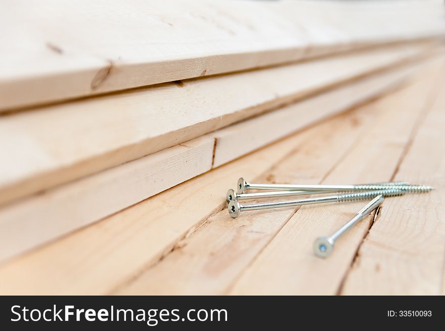 Long screws lie on the wooden boards close-up