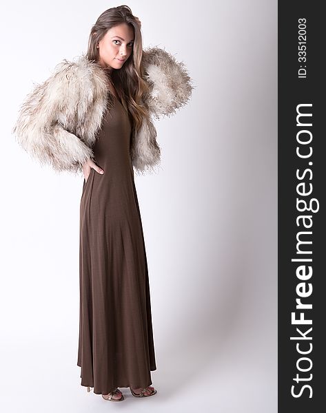 An image of a beautiful woman dressed in a brown dress and beige fur coat. An image of a beautiful woman dressed in a brown dress and beige fur coat