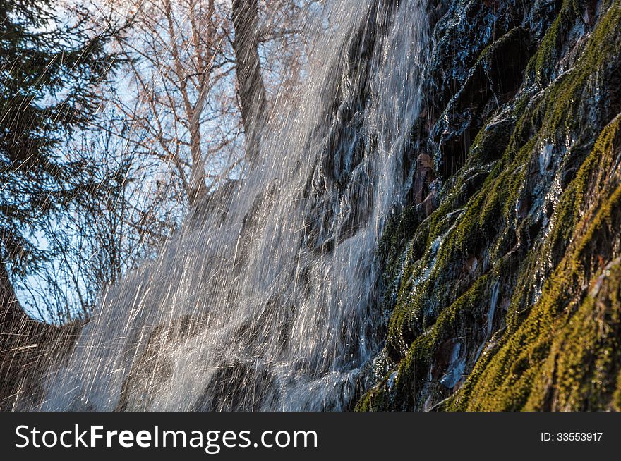 The sun is shining through jets of a waterfall falling from the mountain. The sun is shining through jets of a waterfall falling from the mountain.