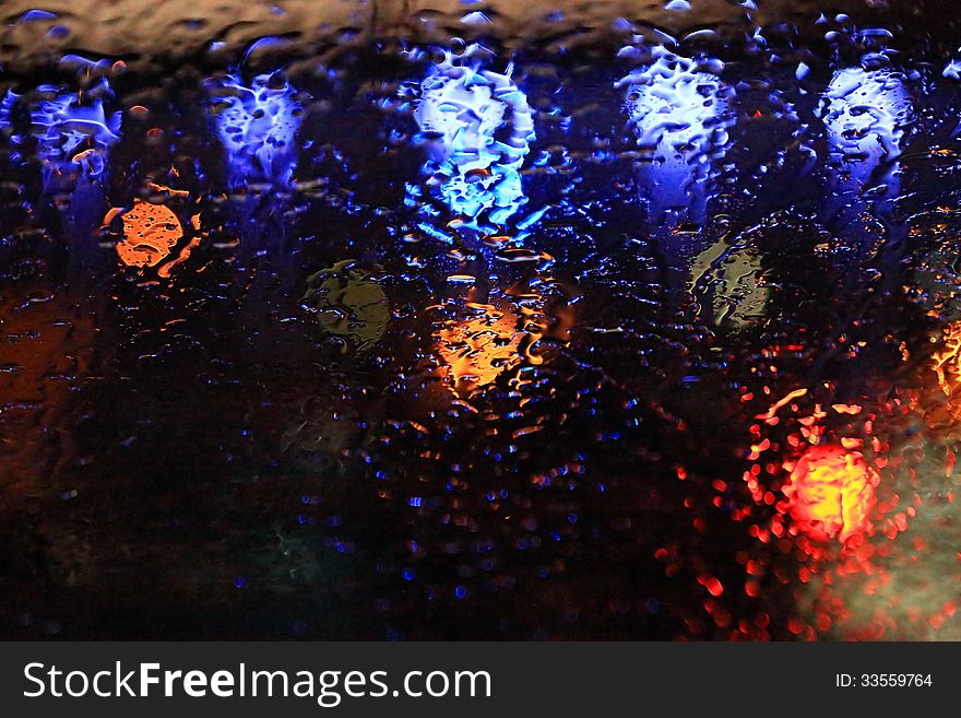 Raindrops on the glass over defocused street lights in the night
