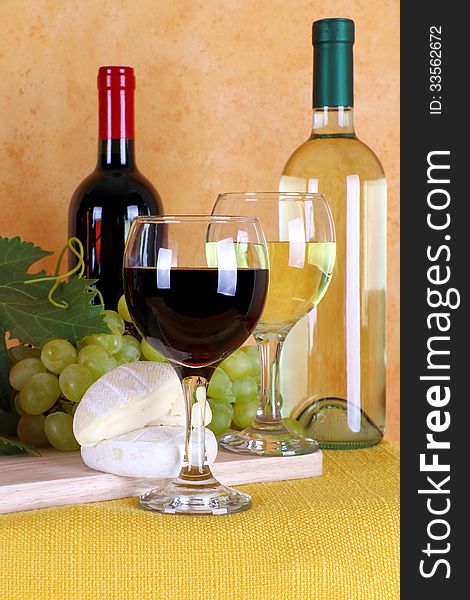 Bottles of red wine, white wine with typical Italian cheese and bunch of grapes and wine glasses in the foreground. Bottles of red wine, white wine with typical Italian cheese and bunch of grapes and wine glasses in the foreground