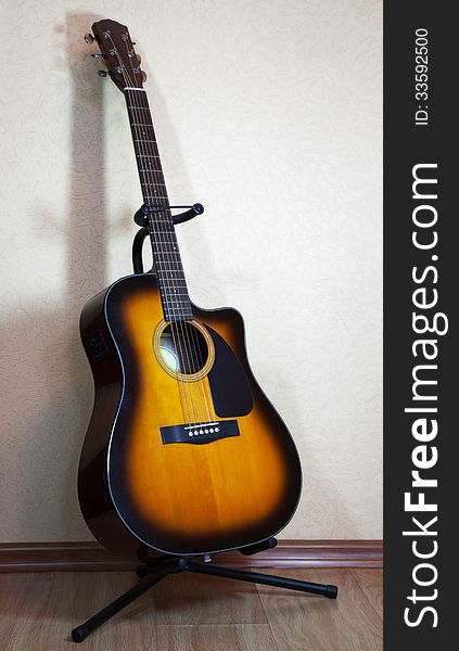 Six-string acoustic guitar on a stand on light background