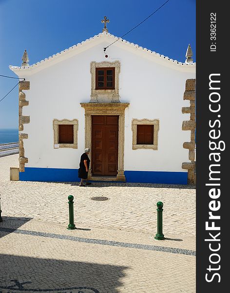 Old woman in black dress is going to the white, small church by the ocean. Old woman in black dress is going to the white, small church by the ocean.