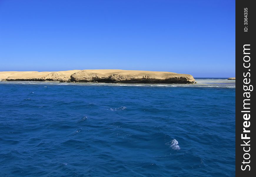 The sandy island located at ocean, among small waves