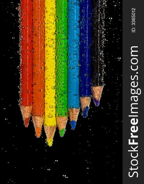 Brightly colored pencils in clear, bubbly liquid. Black background. Brightly colored pencils in clear, bubbly liquid. Black background.