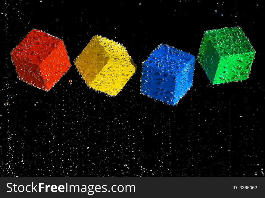Four brightly colored cubes floating in a clear bubbly liquid on a black background. Four brightly colored cubes floating in a clear bubbly liquid on a black background.