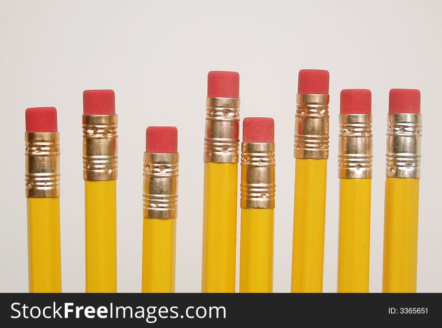 Close-up of eight yellow pencils with pink erasers, isolated against white