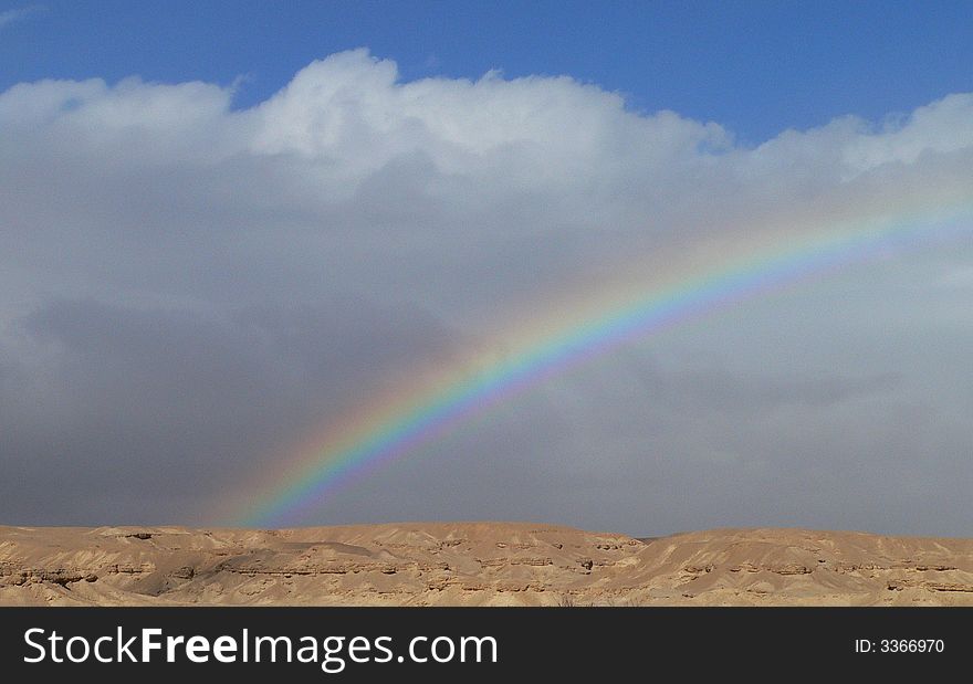 A strong rainbow was created after some rain fall in the desert. Clouds and rainbow. Some blue sky. A strong rainbow was created after some rain fall in the desert. Clouds and rainbow. Some blue sky