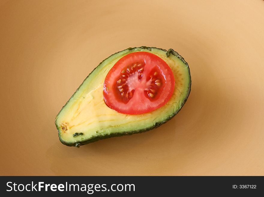 Tomato slice in a cut open Avacado on a yellow plate. Tomato slice in a cut open Avacado on a yellow plate