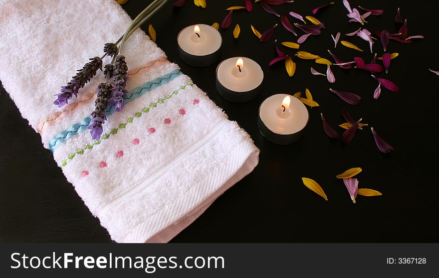 Candles and petals on a brown surface next to a hand towel