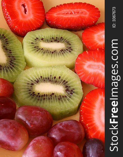 Colourful sliced and whole fruits on a yellow plate. Colourful sliced and whole fruits on a yellow plate