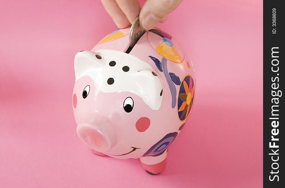 Piggy bank on pink background with hand inserting a silver coin