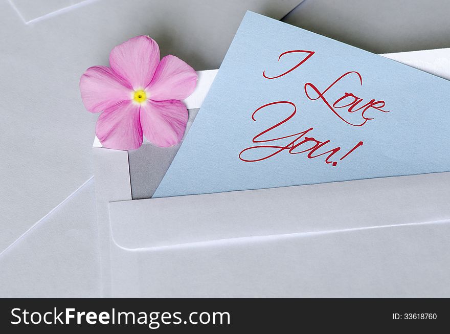A pink flower over a sticky note having written the I Love You text