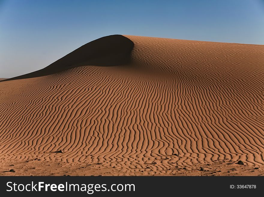 As the strong desert winds blow the cinnamon-colored sand into a tall whipped topping like wave, the smaller breezes at the surface cause endless squiggly longitudinal/linear lines, all contrasting beautifully with the clear blue sky. As the strong desert winds blow the cinnamon-colored sand into a tall whipped topping like wave, the smaller breezes at the surface cause endless squiggly longitudinal/linear lines, all contrasting beautifully with the clear blue sky.