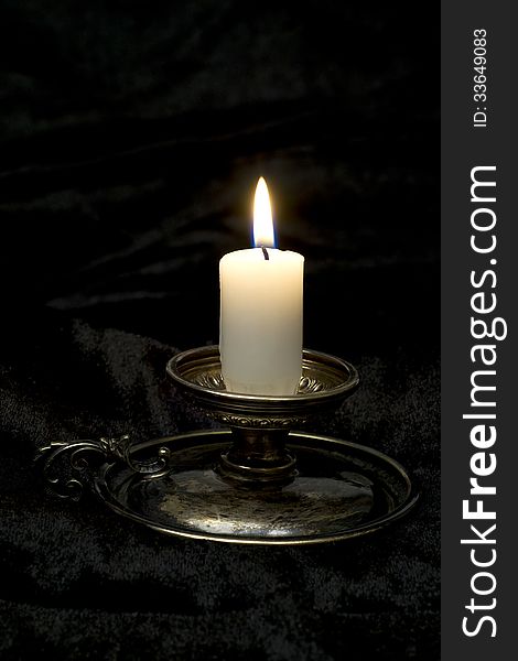 Old time candlestick with burning candle, black velvet background