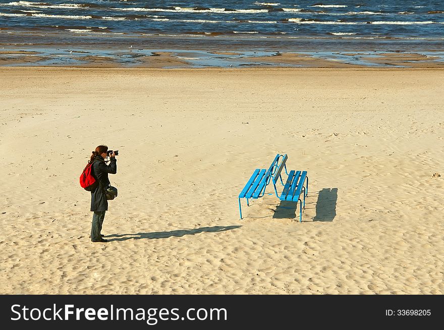 Girl photographer on the sea sandy beach photographs bench