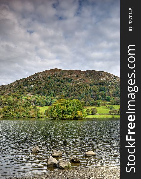 A view of Rydal Water in the English Lake District. There are rocks on the shore and Stratocumulus cloud fills the sky