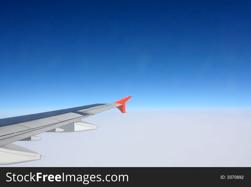 Wing of flying airplane above clouds