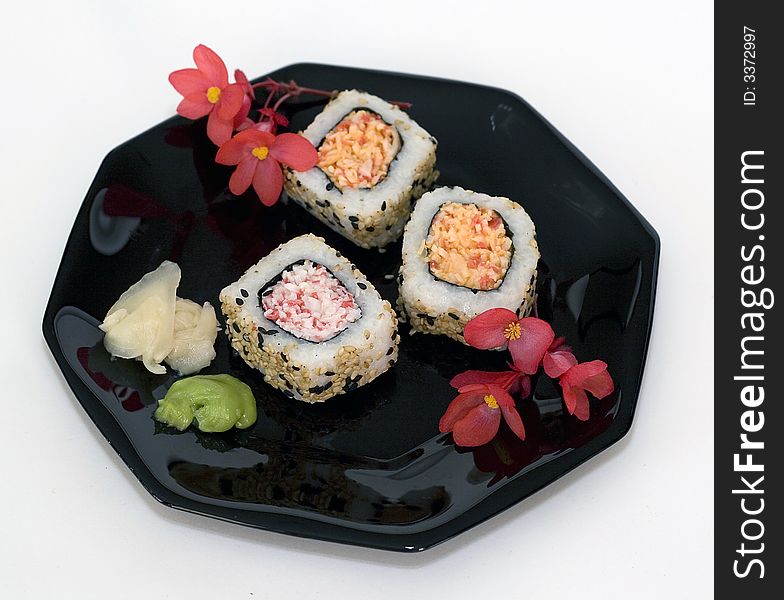 Three pieces of sushi on a black plate.  Wasabi, ginger shown as garnishes.  Red flowers. Three pieces of sushi on a black plate.  Wasabi, ginger shown as garnishes.  Red flowers.