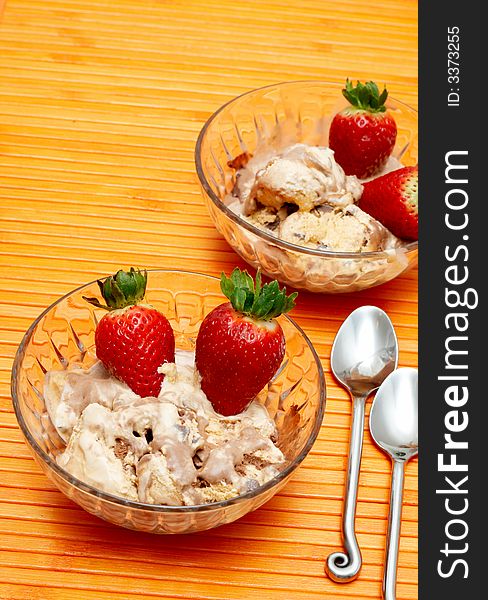 Chocolate ice-cream and strawberries in crystal bowls on orange background