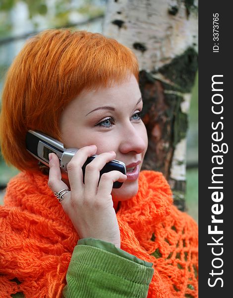 Young red-haired woman in red scarf is talking in mobile-phone. Young red-haired woman in red scarf is talking in mobile-phone