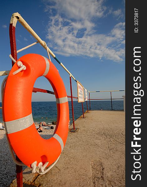 Orange lifebuoy ring on  sea beach on background of  blue sky