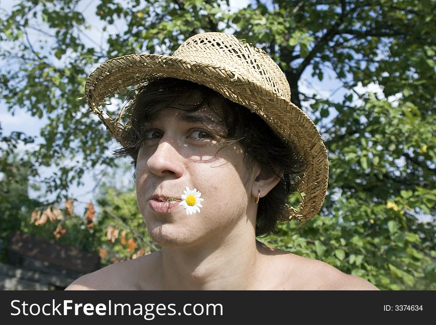 The young man in a garden with a camomile in lips and a straw hat. The young man in a garden with a camomile in lips and a straw hat