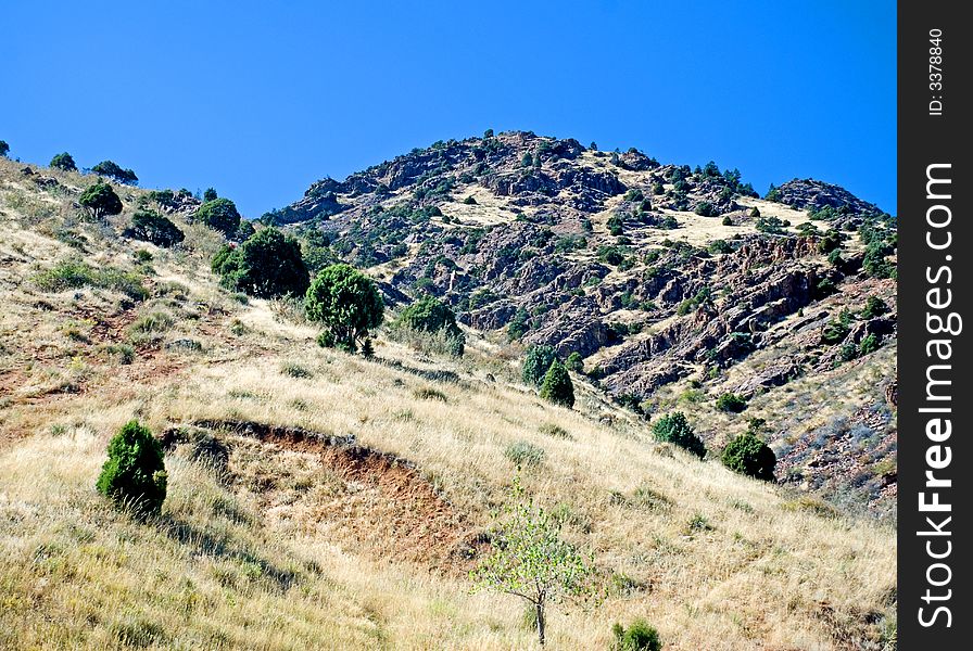 A rocky hill and dry meadow with deep blue sky