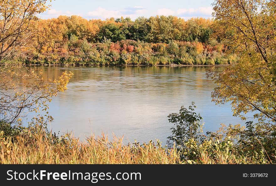 Colorful autumn river framed by trees on near shore.