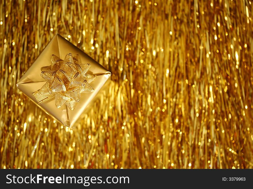 A Christmas box - a golden cube with golden ribbon placed diagonally over golden strings background. A Christmas box - a golden cube with golden ribbon placed diagonally over golden strings background.