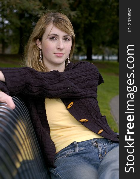 Young beautiful teen outdoors at the park with a different view, pose, scarf, and black sweater. Has a fall or winter season look.