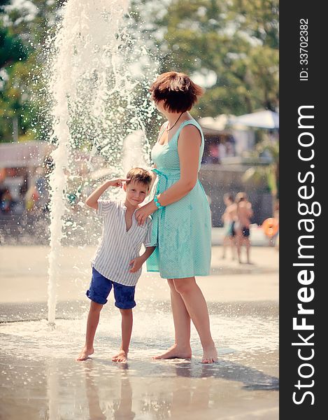 Mother in a turquoise dress with a young son playing at the fountain. Mother in a turquoise dress with a young son playing at the fountain
