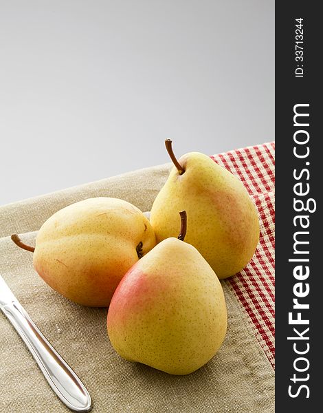 Three ripe pears on a linen napkin on a gray background