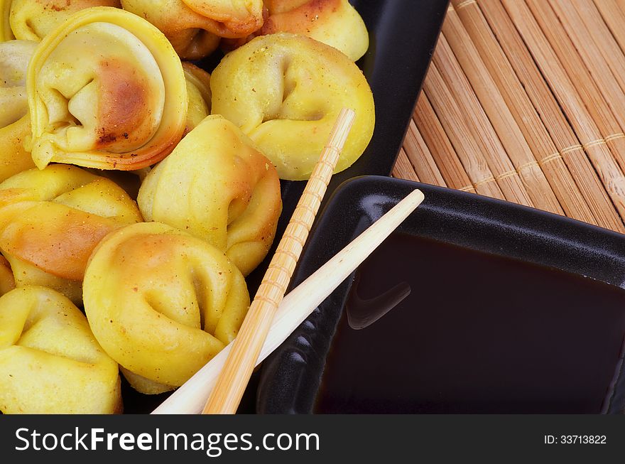 Delicious Fried Crispy Dumplings with Soy Sauce and Chopsticks closeup on Straw mat background