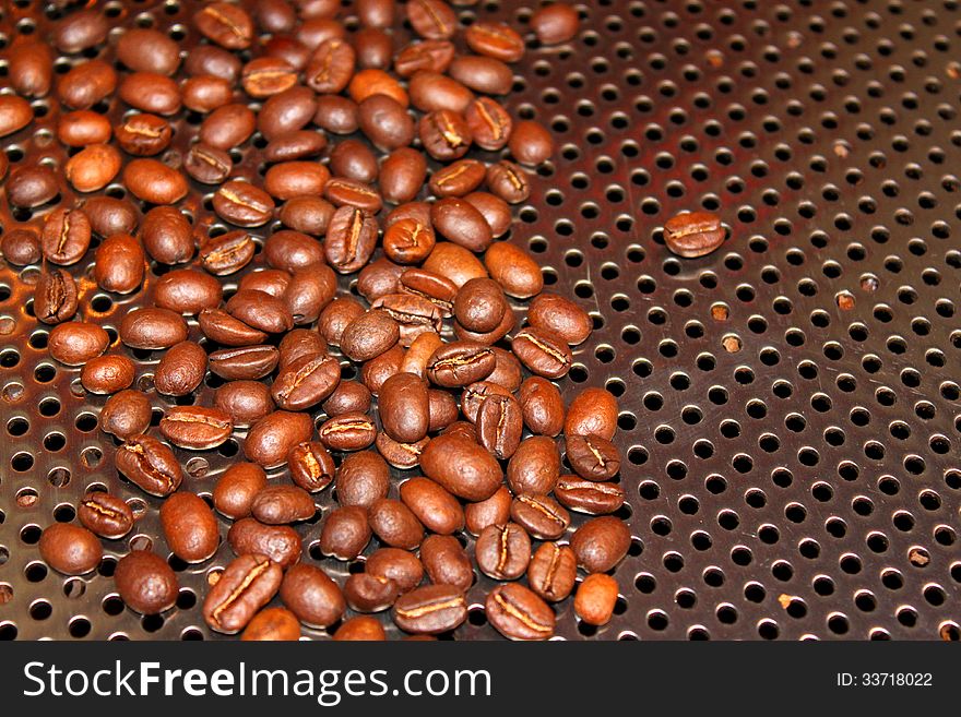 Roasted coffee beans on stainless steel background with holes for ventilation