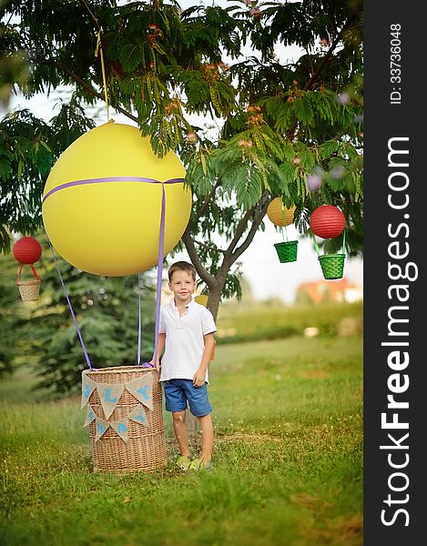 On the green grass boy stands near a hot air balloon with a basket