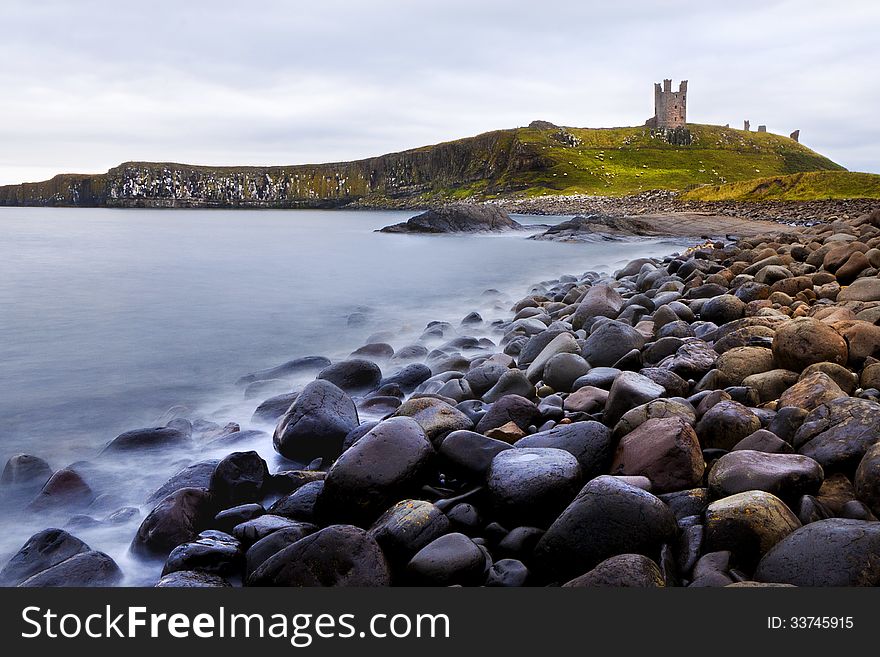 View of Dunstanburgh Castle with large pebbles and stones in foreground