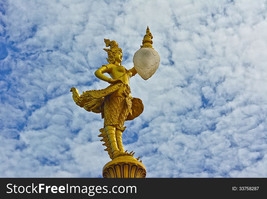 Gold kinnaree statue with lantern and cloudy sky