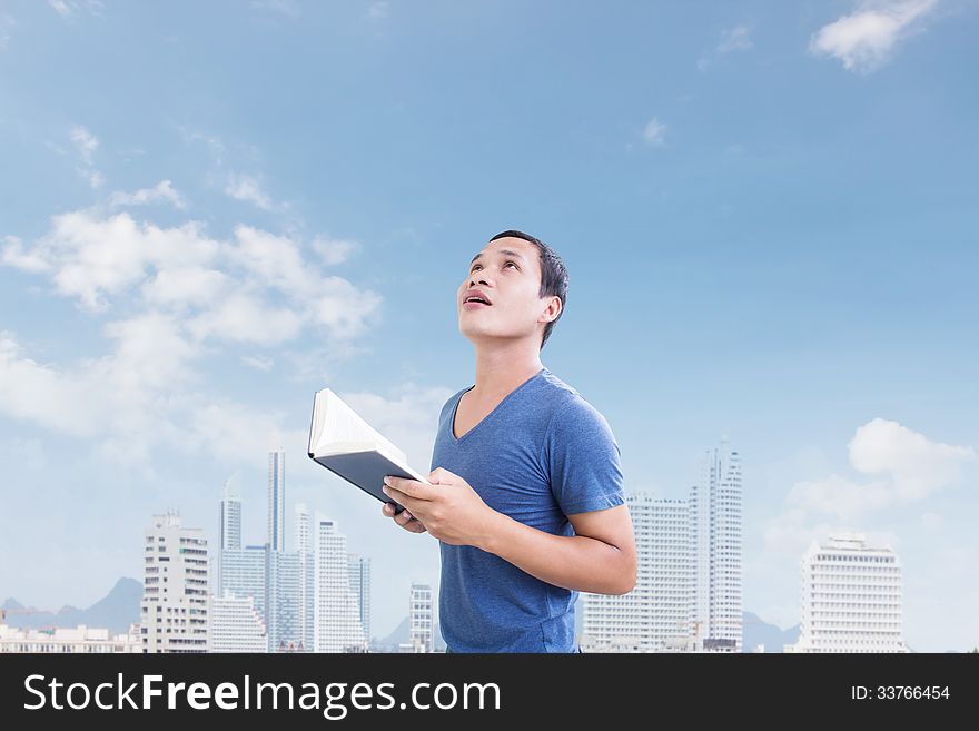 Man Holding Book Looking Up Above With City Background. Man Holding Book Looking Up Above With City Background