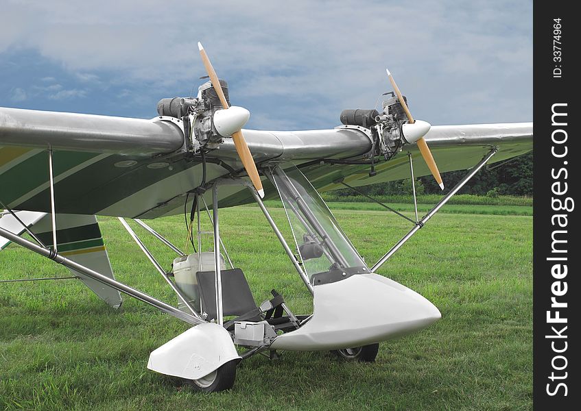 Close-up of a twin engine open cockpit ultralight aircraft sitting on the ground in a field of grass. Close-up of a twin engine open cockpit ultralight aircraft sitting on the ground in a field of grass.