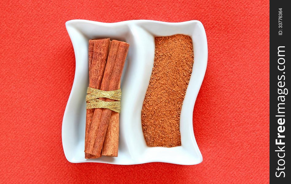 Cinamon bounded sticks bandaged with golden ribbon and powder of cinnamon on a white dish. Cinamon bounded sticks bandaged with golden ribbon and powder of cinnamon on a white dish.