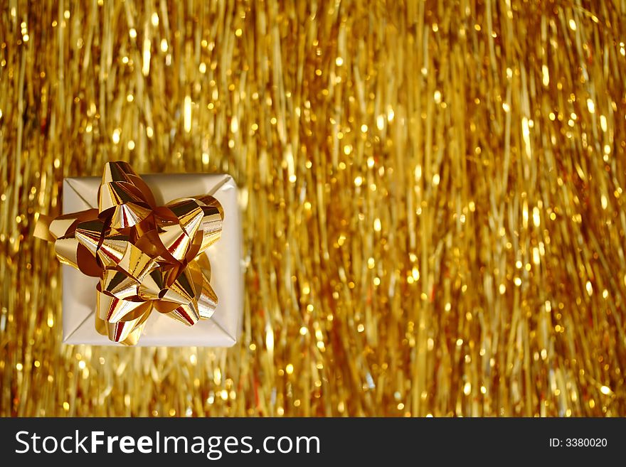 A Christmas box - a slver cube with golden ribbon placed on golden glittering lametta strings. A Christmas box - a slver cube with golden ribbon placed on golden glittering lametta strings.