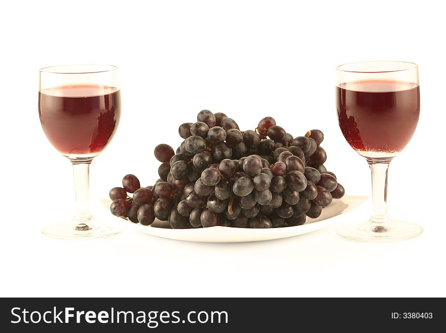 Two glasses of red wine and grapes isolated on white .