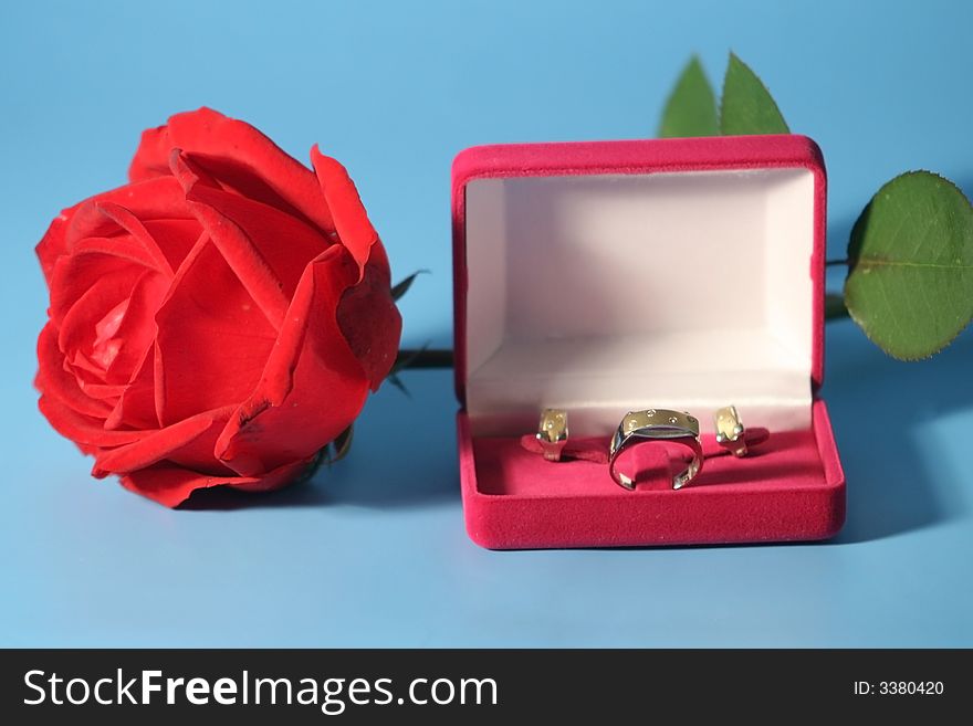 Red rose and a box with gold jewelry on a blue background. Red rose and a box with gold jewelry on a blue background.