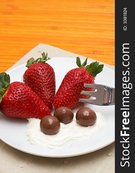 Three strawberries with chocolate balls lying in cream on white saucer. Three strawberries with chocolate balls lying in cream on white saucer