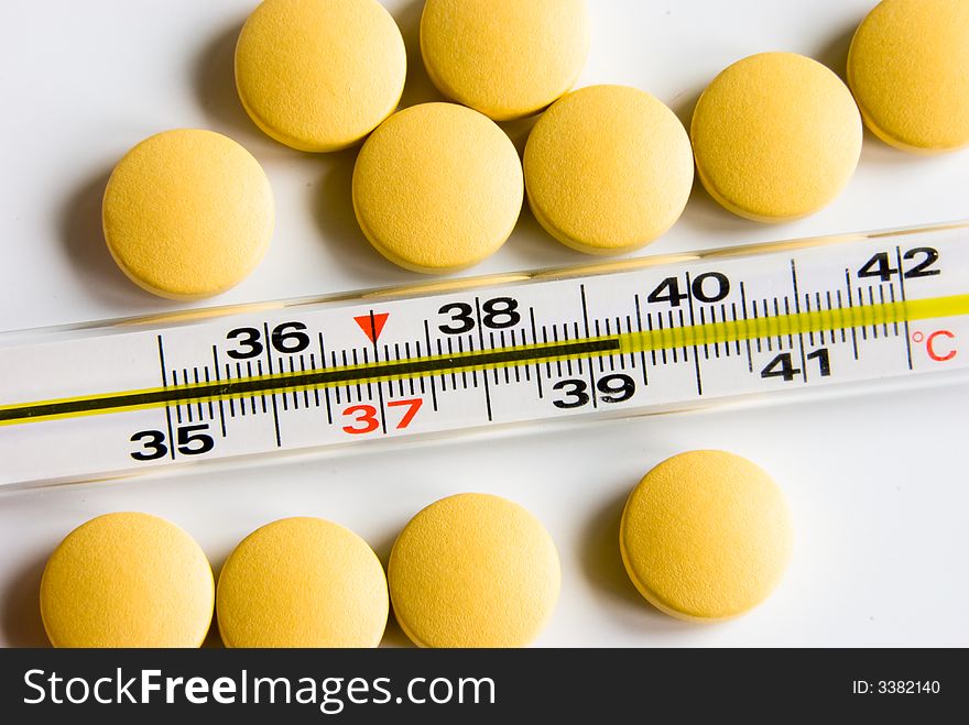 Medical thermometer indicated high temperature and yellow pills over white background. Medical thermometer indicated high temperature and yellow pills over white background