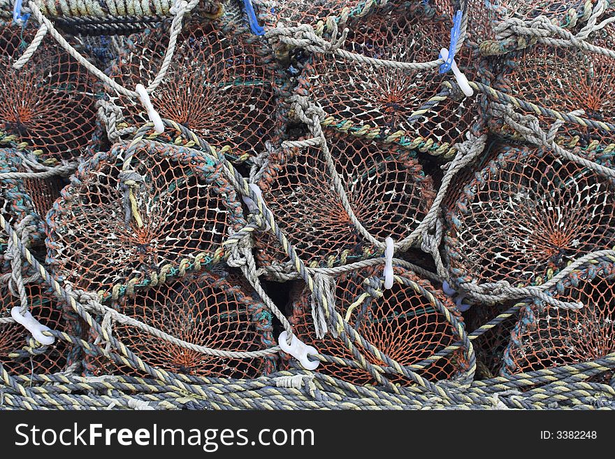 Old and well-used lobster pots stacked neatly on the quayside at a fishing port.